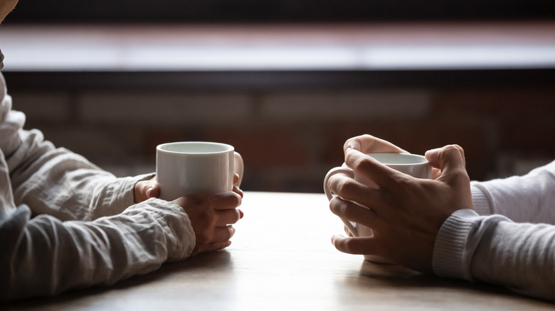 two people sitting at a table, holding cups, while on a date