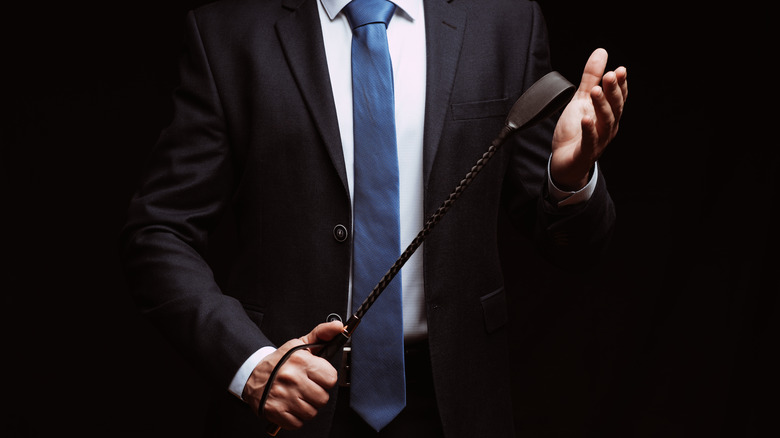 Man in a suit holding a whip