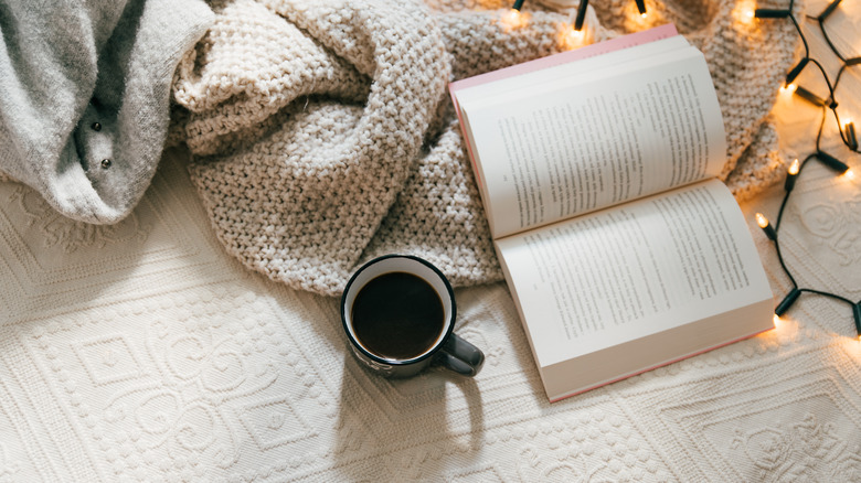 Top view of a book open on a bed with a cup of coffee next to it