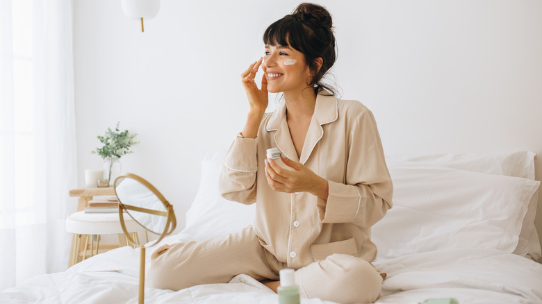 Woman putting a cream face mask on in bed