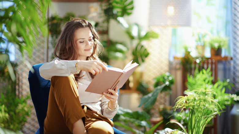 A woman reading while surrounded by houseplants 