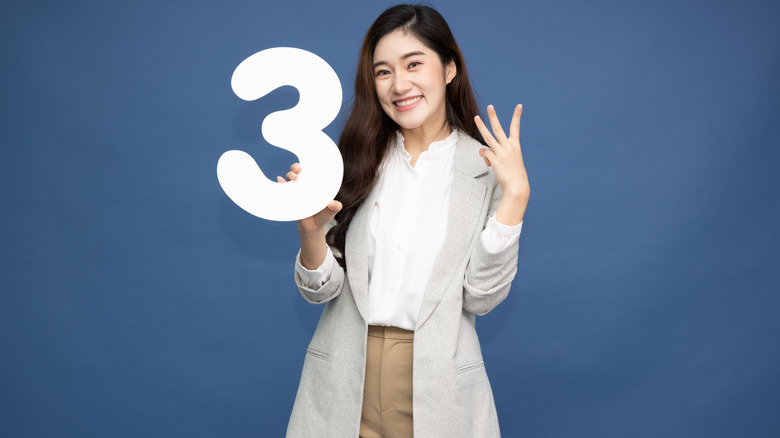 woman holding up a number three