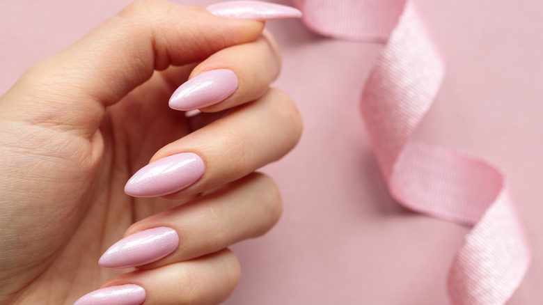hand with long pink nails and pink ribbon in the background