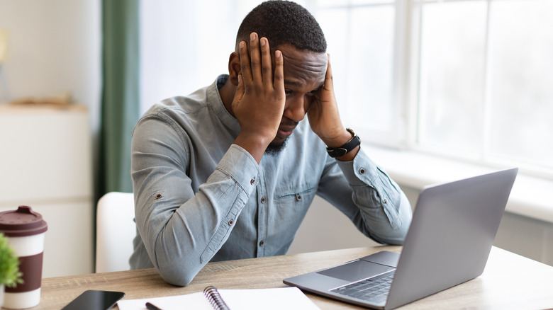 A man sitting at a work desk with his hands over his ears looking stressed