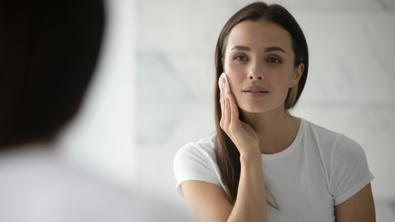 Woman looking at herself in the mirror as she removes her makeup