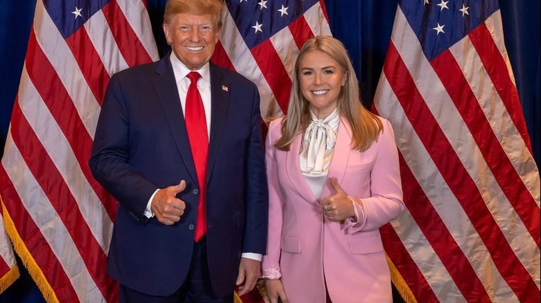 President Donald Trump and Karoline Leavitt pose for a photo together in front of three american flags