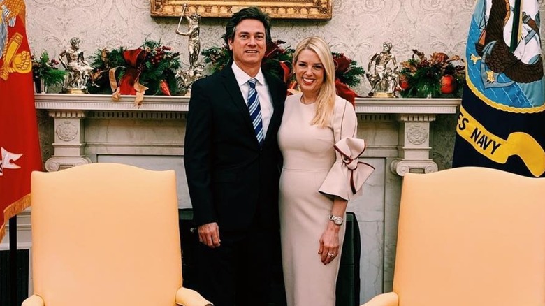 White House Press Secretary Pam Bondi pictured ten days before Christmas wearing a beige, form-fitting dress, with a man stood on her left
