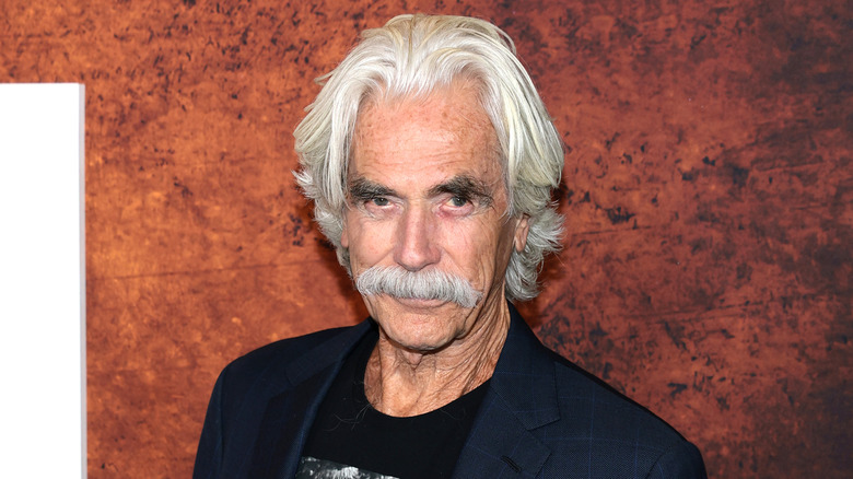 Sam Elliott in front of a red background