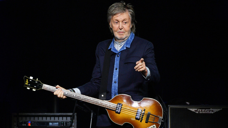 Paul McCartney holding a guitar while pointing a finger at someone in the audience
