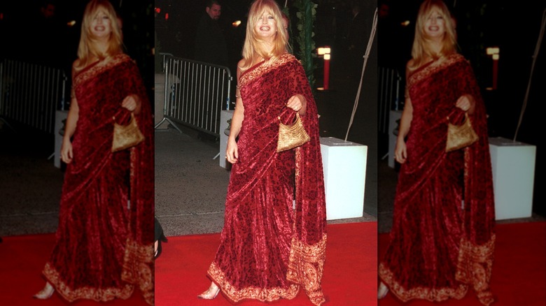Goldie Hawn walking outside wearing a red velvet sari style dress