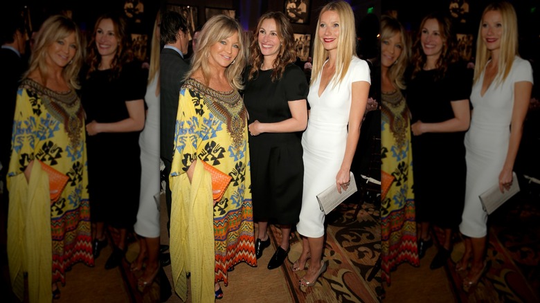 Goldie Hawn in a yellow tunic posing with Julia Roberts and Gwyneth Paltrow, who are dressed in simple black and white dresses