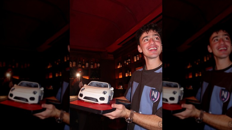 Ben Bader holding a miniature white car in a dimly lit room