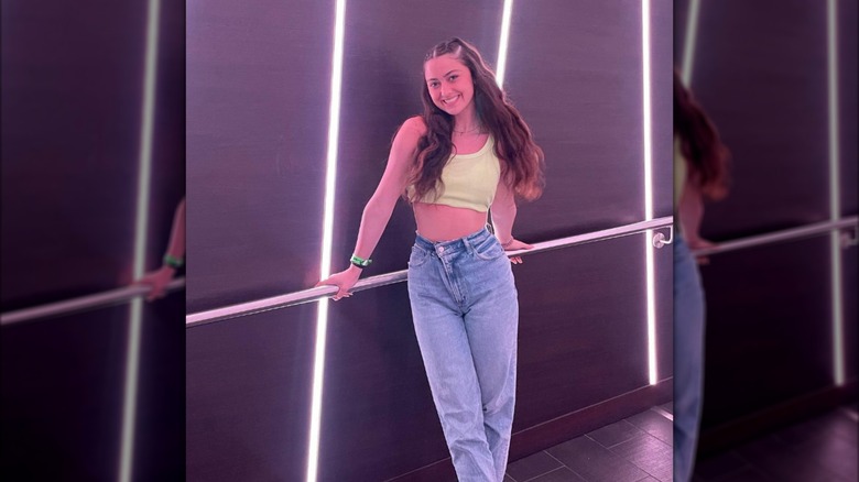 Kailia Posey in a yellow crop top and jeans leaning against a railing