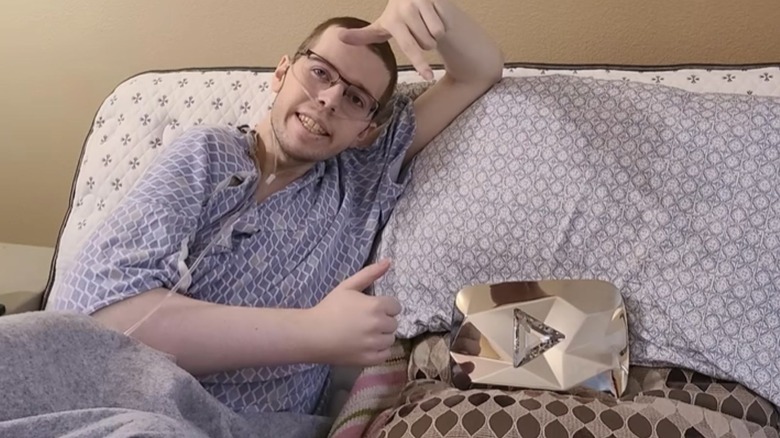 Technoblade lying on a bed in a hospital gown with a YouTube diamond play button beside him