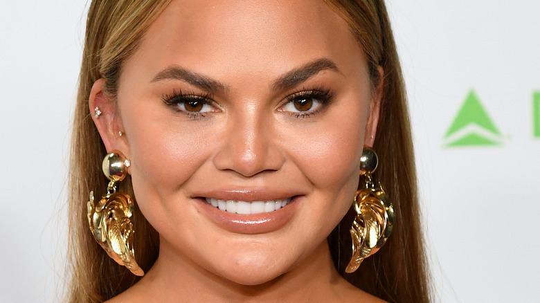 Chrissy Teigen smiling with large gold earrings