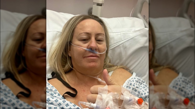 Gill Catchpole in a hospital bed giving a thumbs up 