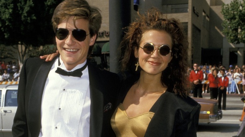 Jason Bateman in a tux and sunglasses and Justine Bateman in gold dress with black jacket and sunglasses on red carpet