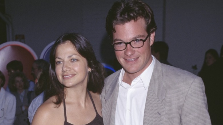 Justine Bateman in black sleeveless top and pants with arm around Jason Bateman in glasses wearing white shirt and gray sportcoat