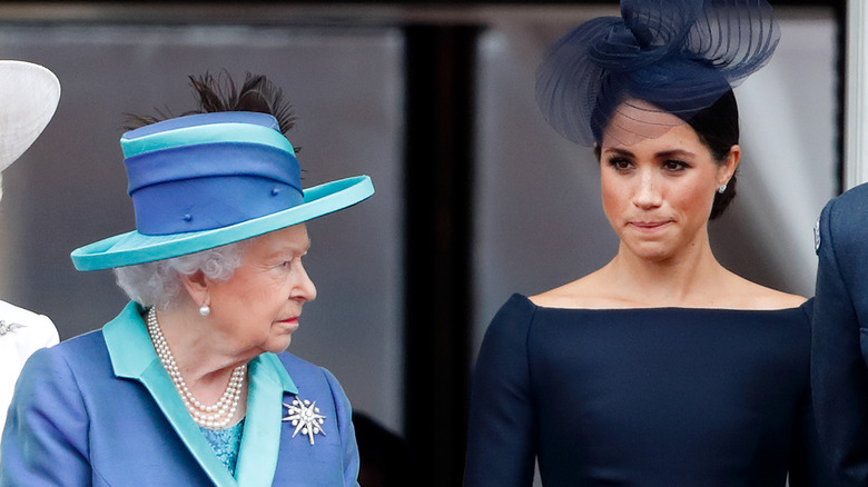 Queen Elizabeth looking stern while Meghan Markle presses her lips together