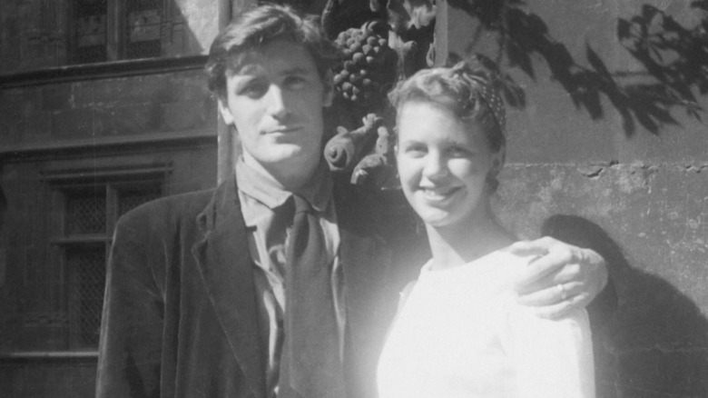 Ted Hughes looking serious with his arm around a smiling Sylvia Plath