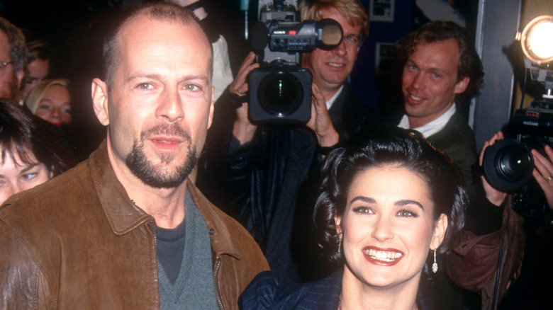 Demi Moore and Bruce Willis smiling in 1992 with cameramen in the background.