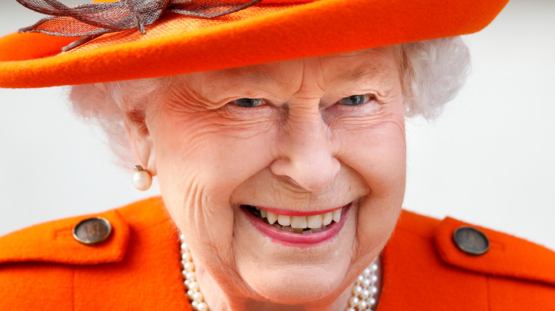 Queen Elizabeth wearing a bright orange outfit with matching top hat