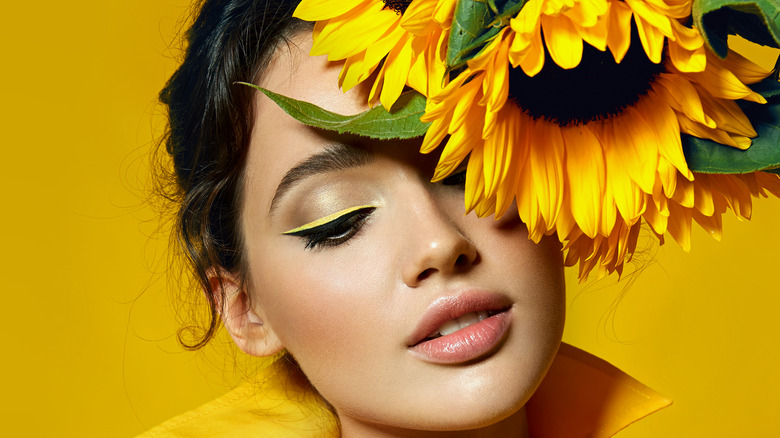 A woman with yellow eyeliner holding a sunflower