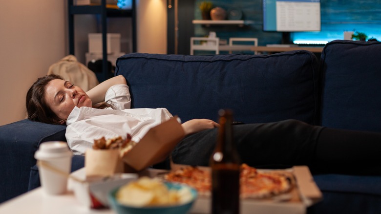 Person sleeping on sofa surrounded by food