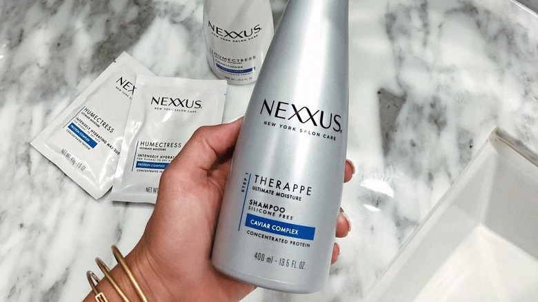 A woman holding  a bottle of Nexxus shampoo