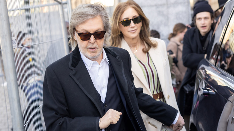 Paul McCartney walking in front of Nancy McCartney as a man in a beanie looks on