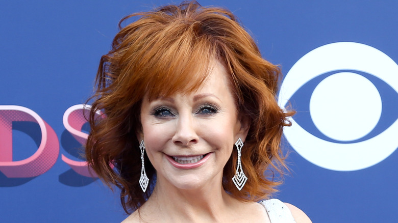 Reba McEntire smiling in front of blue backdrop