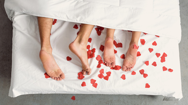 A couple's feet in bed surrounded by red hearts