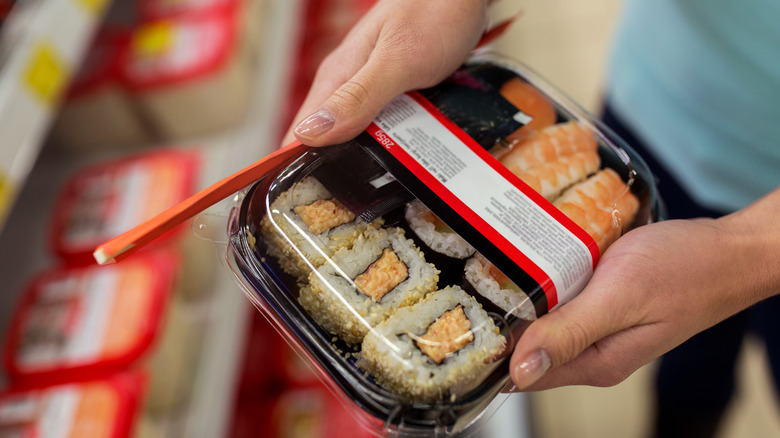 Hands holding packaged sushi rolls