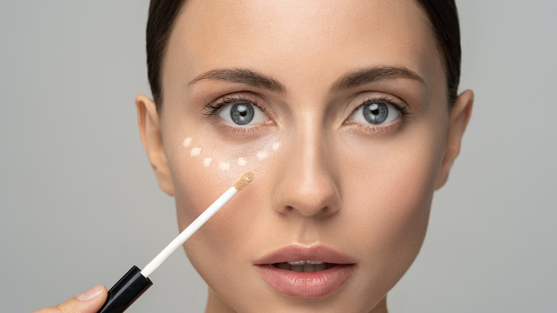 A woman putting on concealer under her eyes