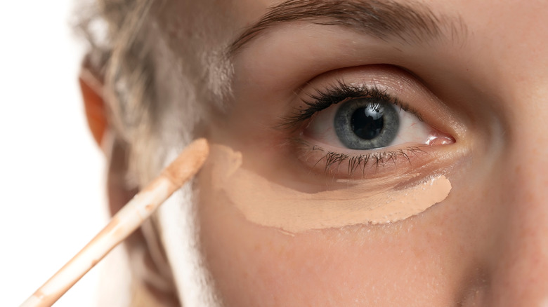 A woman putting on concealer under her eye