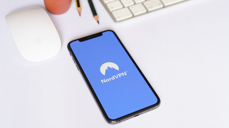 NordVPN open on phone next to keyboard, mouse and pencils