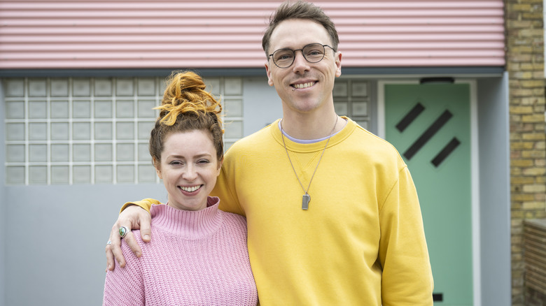 A couple wearing pastels standing in front of a house