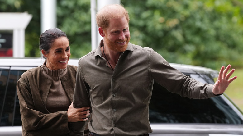 Meghan Markle and Prince Harry smiling and wearing brown outfits.