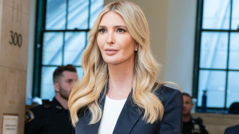 Ivanka Trump with pleasant resting face inside a building with windows, wearing a white shirt and blue blazer
