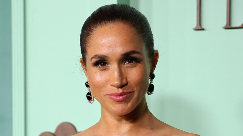 Meghan Markle smiling while posing with her hair pulled back and black chandelier earrings