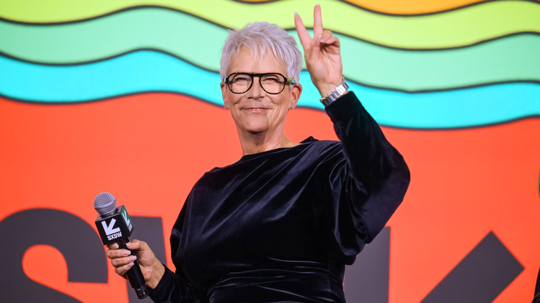 Jamie Lee Curtis smiling and throwing up a peace sign on stage at SXSW
