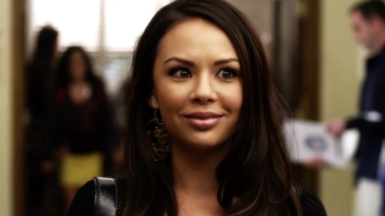 Janel Parrish as Mona in "Pretty Little Liars" standing in a school hallway