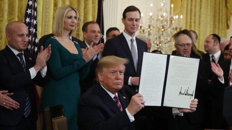 Donald Trump holding a signed executive order with Ivanka Trump and Jared Kushner in the background