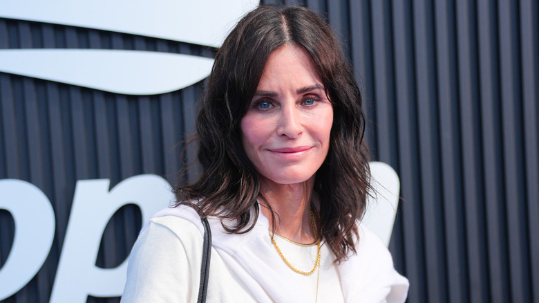 Courteney Cox in all white in front of a barred black background.
