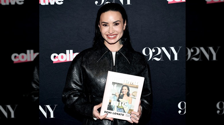 Demi Lovato smiling and holding her cookbook