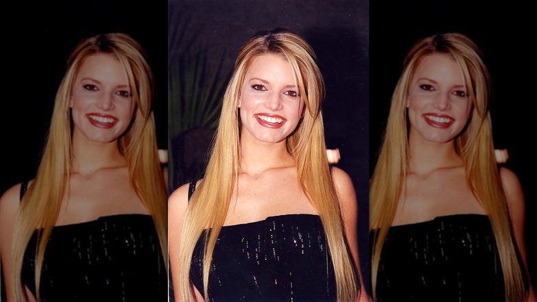 Young Jessica Simpson in a black dress in front of greenery.