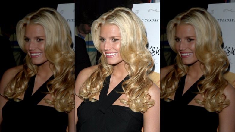Jessica Simpson in a black dress in front of a white sign.