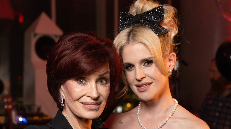 image of Sharon Osbourne and Kelly Osbourne leaning their heads together and smiling at the camera.