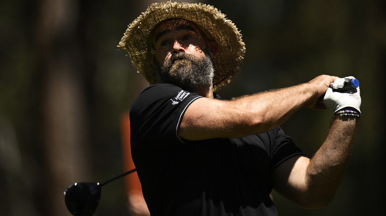 Jason Kelce in full swing with a straw hat on and a golf club in hand.