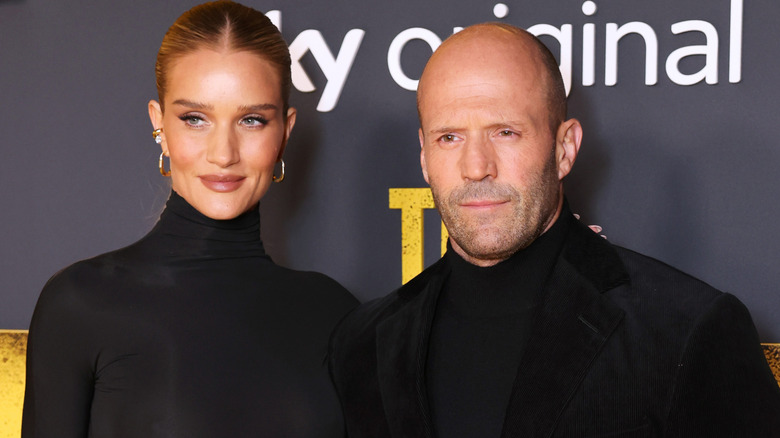 Rosie Huntington-Whiteley and Jason Statham together, both wearing black and looking at a camera to the side